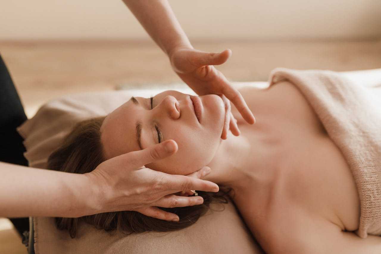 a-woman-having-a-massage-6663361 Woman receiving a soothing facial massage, promoting relaxation and wellness.